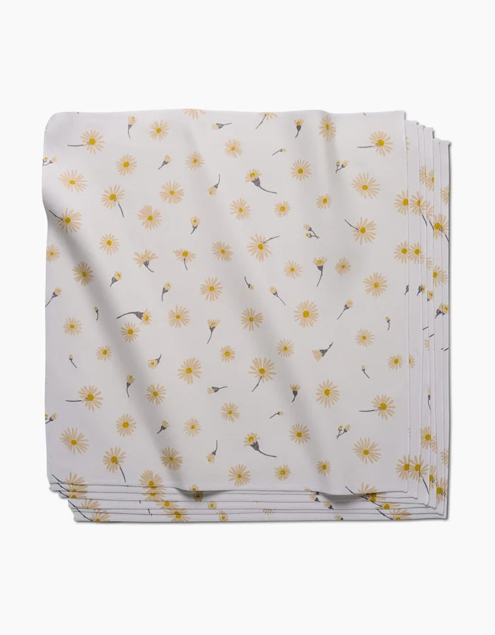 The Daisy Dust dinner napkin by Hufton Studio is neatly folded, crafted from recycled Geosuede fabric, and features a pattern of small yellow daisies and scattered floral sprigs.