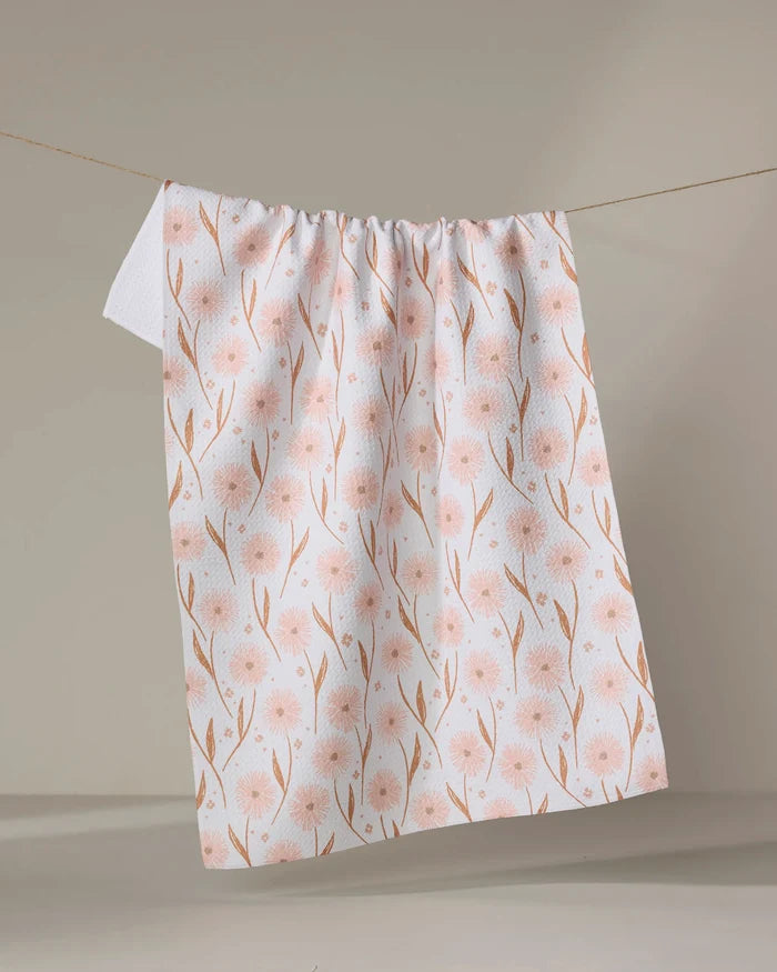 The Daisy Pop tea towel by Hufton Studio, featuring a light pink floral design on white, hangs on a clothesline against a neutral background. Its quick-drying fabric makes it both stylish and practical for any kitchen.