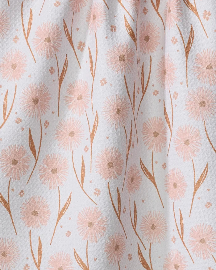 Close-up of the Hufton Studio Daisy Pop tea towel featuring a delicate pattern of light pink dandelion-like flowers and curved leaves on softly draped, textured white Geoweave fabric.
