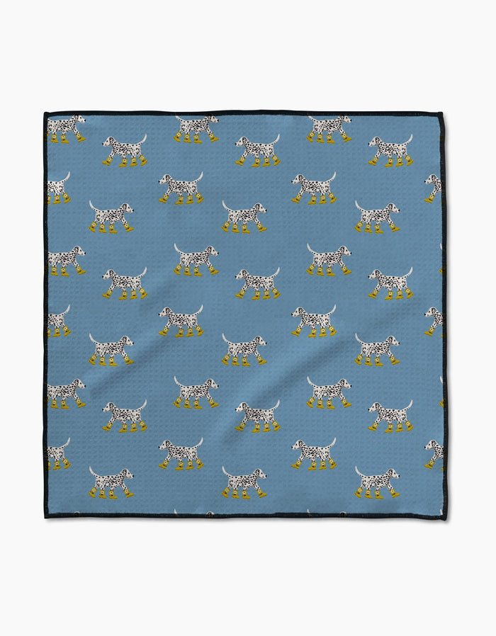 The Geometry Dalmatian In Boots Blue Paw Towel features a blue Geoweave cloth with white spotted dogs in yellow boots, arranged in rows facing both ways, and finished with black borders for a stylish touch.