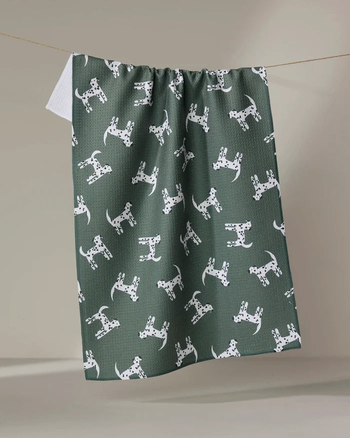 The Coit Creative "Dalmatian Dogs" ultra-absorbent green tea towel, featuring a repeating white Dalmatian pattern, is shown hanging on a clothesline against a neutral background.