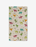 GEOMETRY’s Dancing Dinos Bath Towel, rectangular with a playful dinosaur pattern in green, orange, pink, and blue on cream with grass and rocks. Features ultra-absorbent Geoweave technology and “RAWR!” text near some dinos.