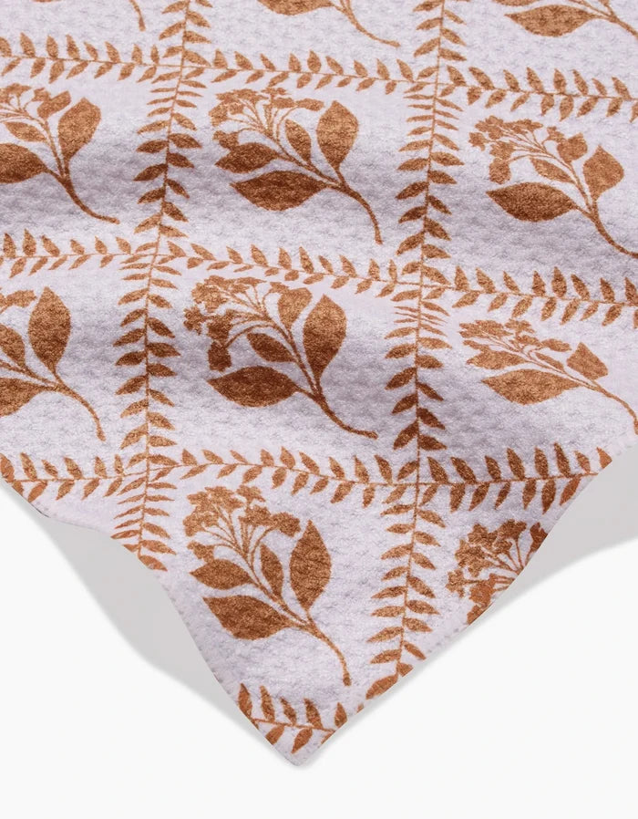 The Dancing Vines towel by Charlie Rowan Designs features a soft, ultra-absorbent fabric with brown botanical leaves and flowers in a grid on a white background, showcased with its finished edge in the corner.