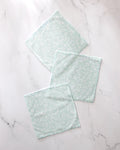 Three Dandy reusable dishcloths by GEOMETRY, featuring a light green and white textured design, are spread out on a white marble surface with their edges slightly overlapping.