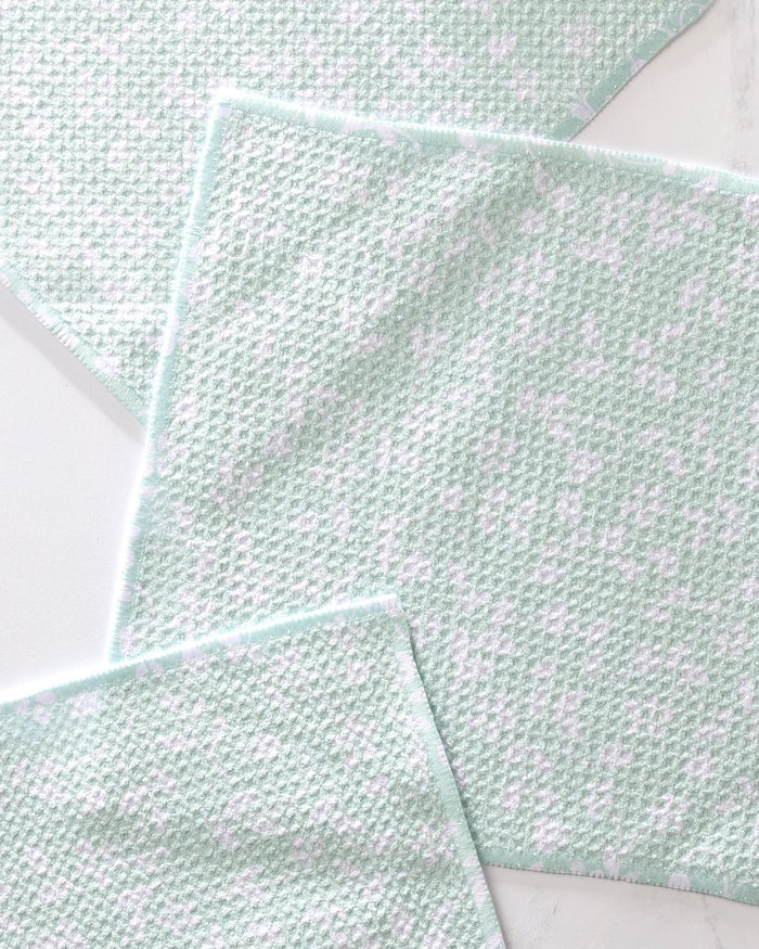 Three Dandy cleaning cloths by GEOMETRY, light green and white with a waffle-like texture and soft white patches, are arranged overlapping on a light surface—an eco-friendly kitchen choice in a reusable dishcloth set.