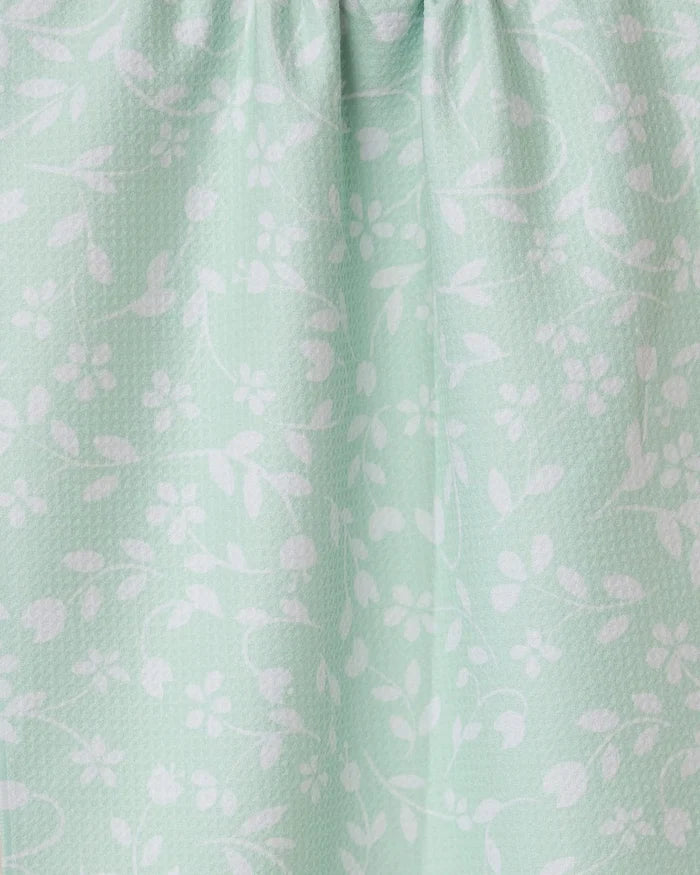 The Dandy kitchen towel by GEOMETRY is light green with white floral and leaf designs. It features a subtle textured pattern and softly gathered fabric at the top for gentle folds.
