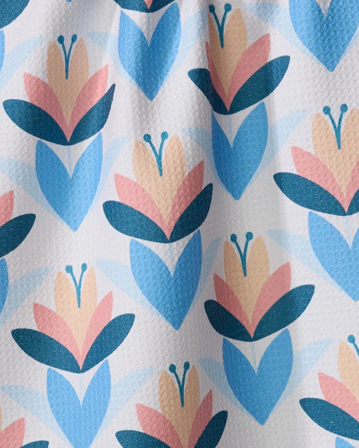 The Daytime Florals tea towel by Blissful Flamingo is made from recycled materials and features a blue, pink, and beige floral pattern with heart-shaped blue leaves and soft pink petals on a white textured background.