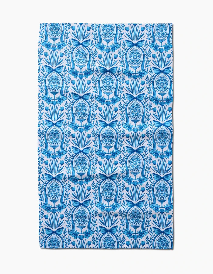 The Sarah Daugherty Delft Blue Easter Egg Damask tea towel features a repeating blue floral and fruit vase pattern with symmetrical, intricate detailing on a white background.
