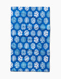 The Delft Blue Easter Eggs tea towel by Sarah Daugherty is rectangular, blue, and made from recycled materials, featuring a repeating pattern of white and blue spheres with geometric and abstract designs.