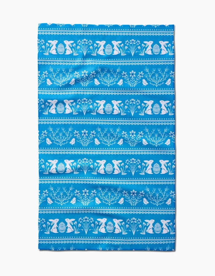 The Delft Blue Easter Stripe towel by Sarah Daugherty is quick-drying and features white horizontal patterns of bunnies, birds, flowers, and decorated eggs in repeating rows on a blue background.
