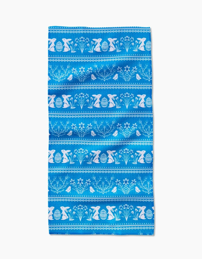 The Delft Blue Easter Stripe by Sarah Daugherty is a Geoweave napkin with blue horizontal stripes and white silhouettes of rabbits, Easter eggs, flowers, and leaves in a repeating pattern.