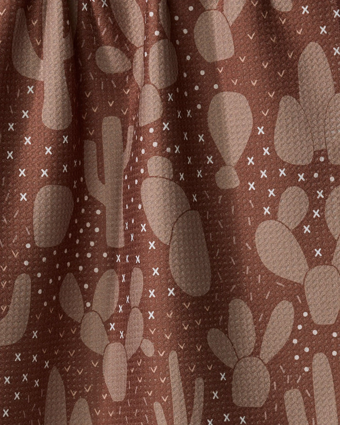 Desert Night by Rosa Kichline: a brown recycled fabric kitchen towel with a textured feel, featuring beige cacti and white X and dot patterns. Drapes beautifully with visible folds—eco-friendly style for your home.