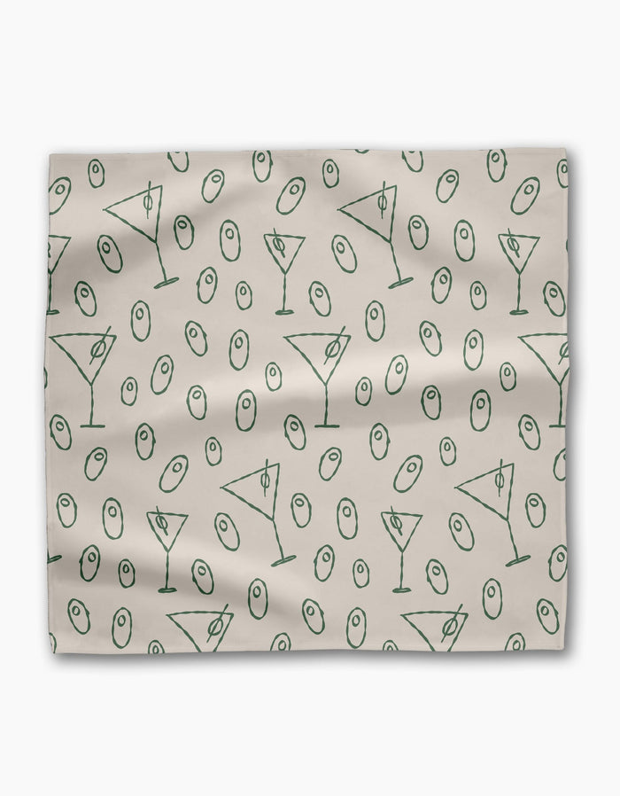 The Dirty Martini dinner napkin set by Rosa Kichline is light beige, made from recycled fabric, and showcases a repeating pattern of green martini glasses and green olives scattered across the surface.