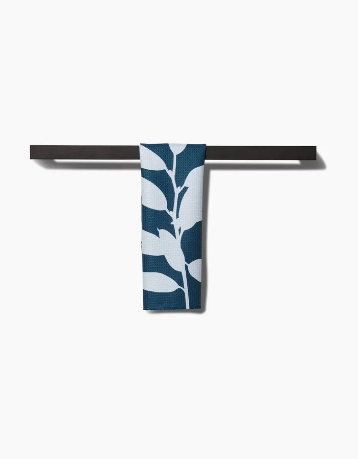 The Doghobble bar towel by PrintedPlant, featuring a bold blue and white leaf design on Geoweave fabric, is displayed neatly over a sleek black towel bar against a plain white background.