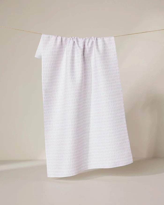 The Geometry Dot Dot Dot Blushed Bergamot towel, ultra-absorbent and white, hangs on a clothesline against a light beige background.