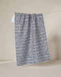 The Geometry Dot Dot Dot Fresh Linen recycled kitchen towel, featuring a black irregular dot pattern on white, hangs from a thin clothesline against a plain beige background.
