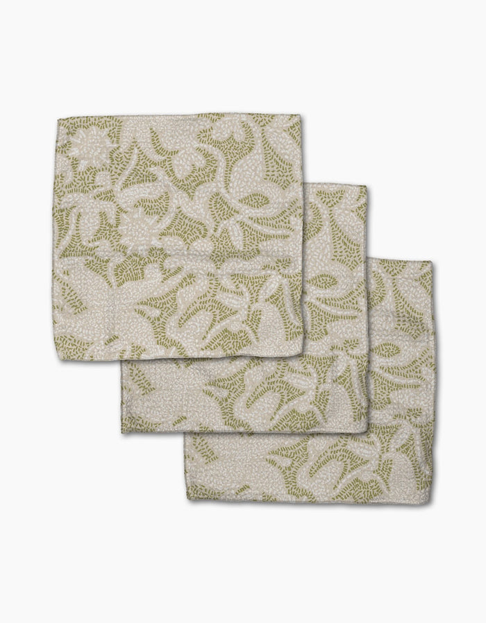Three folded Geometry Dotted Floral Garden napkins, featuring a green botanical pattern on white recycled fabric, are arranged with each napkin slightly overlapping on a plain white surface.