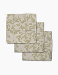 Three folded Geometry Dotted Floral Garden napkins, featuring a green botanical pattern on white recycled fabric, are arranged with each napkin slightly overlapping on a plain white surface.