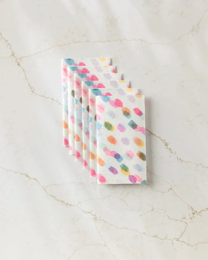 Six stacked GEOMETRY Downpour reusable paper towels in a pastel polka dot pattern are arranged neatly on white marble with beige veining.