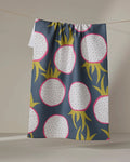 The Lizzie Clark "Dragon Fruit Frolic" tea towel, featuring bold dragon fruit shapes in pink, white, yellow-green, and black on dark blue fabric, dries quickly and hangs on a line.