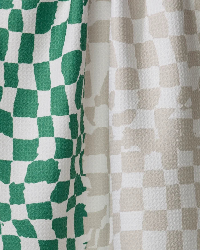 Close-up of Geometry's Dual kitchen towel, featuring ultra-absorbent, soft fabric from recycled materials. Its irregular checkerboard pattern has green and white squares on the left and beige and white on the right, draping naturally.