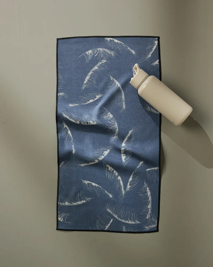 A GEOMETRY Due North Midnight water bottle sits atop an ultra-absorbent towel with a white palm leaf pattern, arranged on a light gray surface.