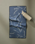 A GEOMETRY Due North Midnight water bottle sits atop an ultra-absorbent towel with a white palm leaf pattern, arranged on a light gray surface.