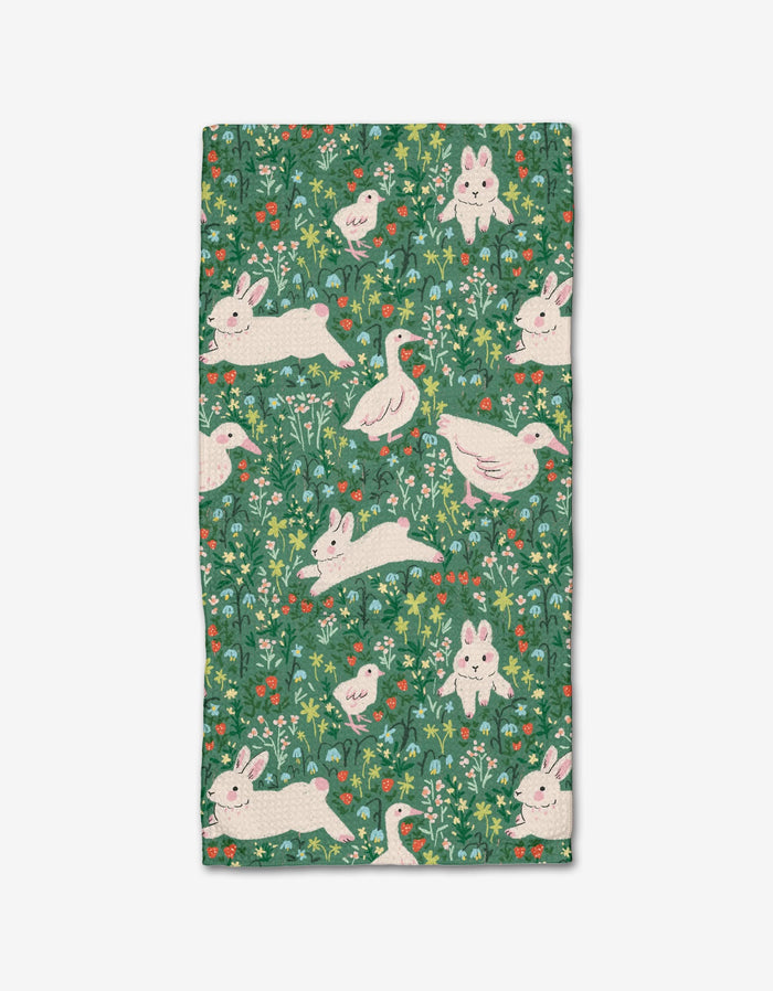 The Easter Meadow bar towel by Janna Sue Design features Geoweave™ fabric with playful white rabbits and ducks, green grass, leafy details, and colorful flowers on a green background with intricate plant motifs.