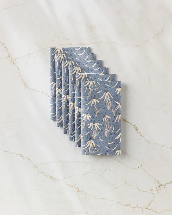 A stack of Katie O'Shea Echinacea blue reusable paper towels with a white floral pattern, neatly arranged on a white marble surface with light brown veining.