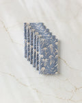 A stack of Katie O'Shea Echinacea blue reusable paper towels with a white floral pattern, neatly arranged on a white marble surface with light brown veining.