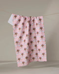 Echo, a quick-drying pink tea towel by Maayan Alper-Swan, displays a repeating bee pattern and hangs on a clothesline against a neutral background.