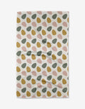 The Egg Hunt tea towel by Charlie Rowan Designs features green, mustard yellow, and pink oval shapes in diagonal rows on textured waffle fabric. Quick-drying and shown on a white background.