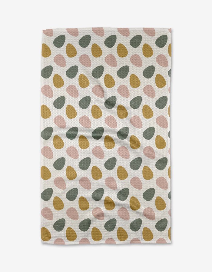 The Egg Hunt tea towel by Charlie Rowan Designs features green, mustard yellow, and pink oval shapes in diagonal rows on textured waffle fabric. Quick-drying and shown on a white background.