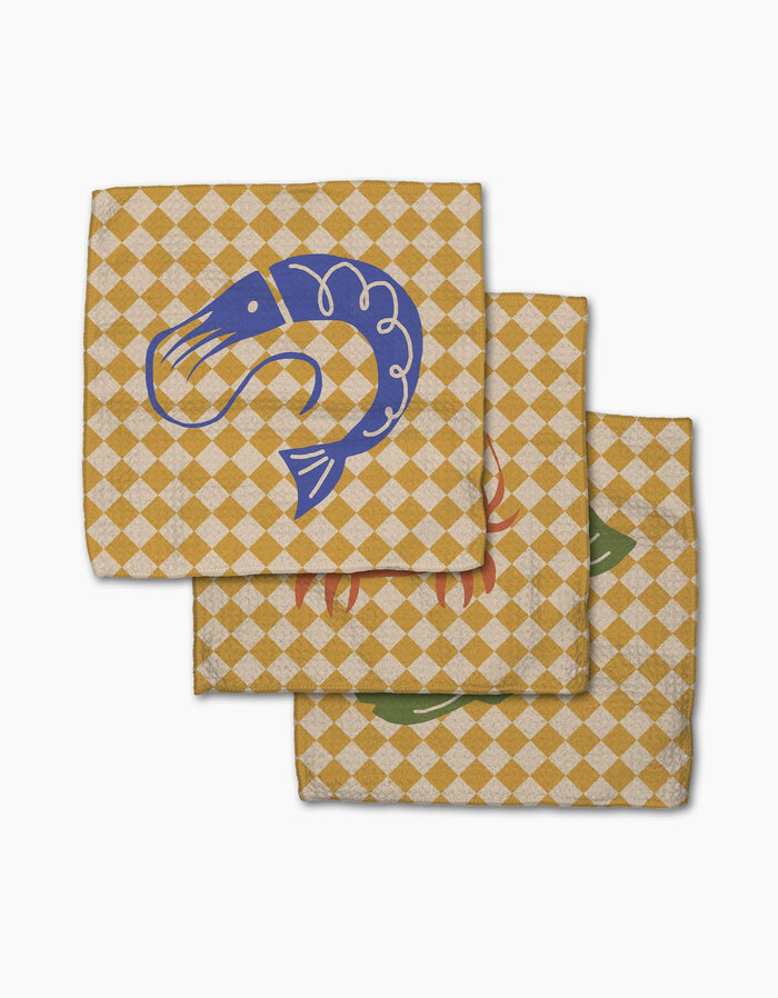 The El Mar Dos dishcloth set by Geometry includes three checkered yellow and white Geoweave napkins, each with a unique seafood illustration—blue shrimp, red lobster, and green fish—for a stylish and absorbent touch.