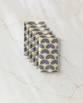 Six Eliza cloth napkins by Amy MacCready, featuring an art deco fan pattern in blue, cream, and gold—an eco-friendly alternative to disposables—are neatly folded and displayed on white marble with beige veining.