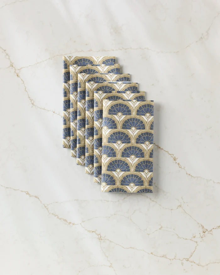 Six Eliza cloth napkins by Amy MacCready, featuring an art deco fan pattern in blue, cream, and gold—an eco-friendly alternative to disposables—are neatly folded and displayed on white marble with beige veining.