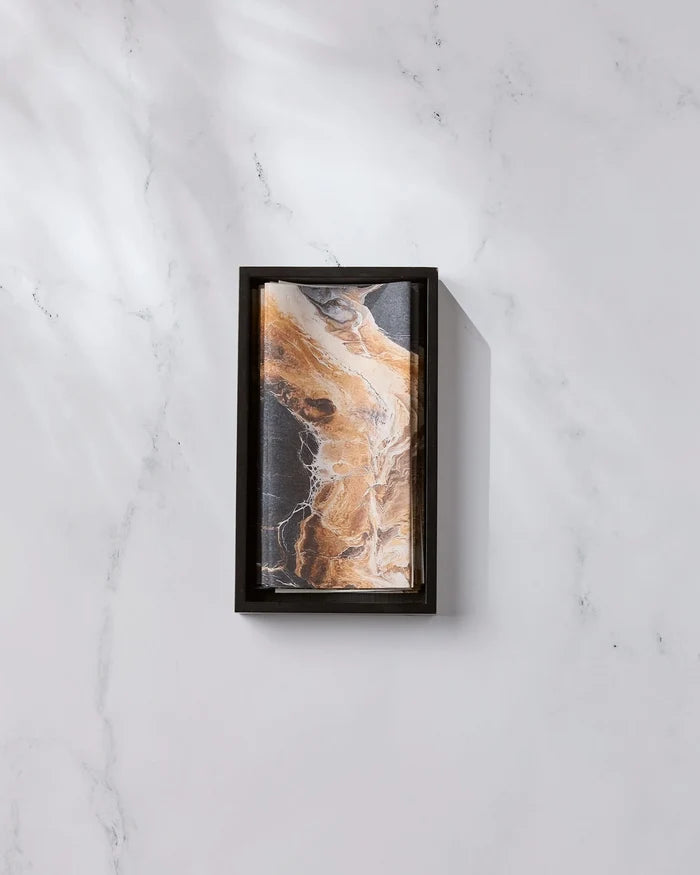 The Emperador by Geometry, featuring a rectangular black frame and an abstract brown, black, and white marble-inspired pattern, rests on a white marble surface with light gray veining as diagonal shadows fall across the scene.