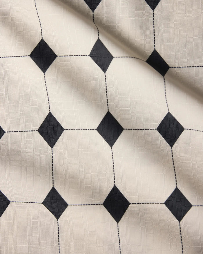 A close-up of Geometrys Espresso Mosaic tablecloth, featuring lightweight cream fabric with a grid of black square dots connected by dashed lines. The fabric offers subtle wrinkles and a soft, inviting texture.