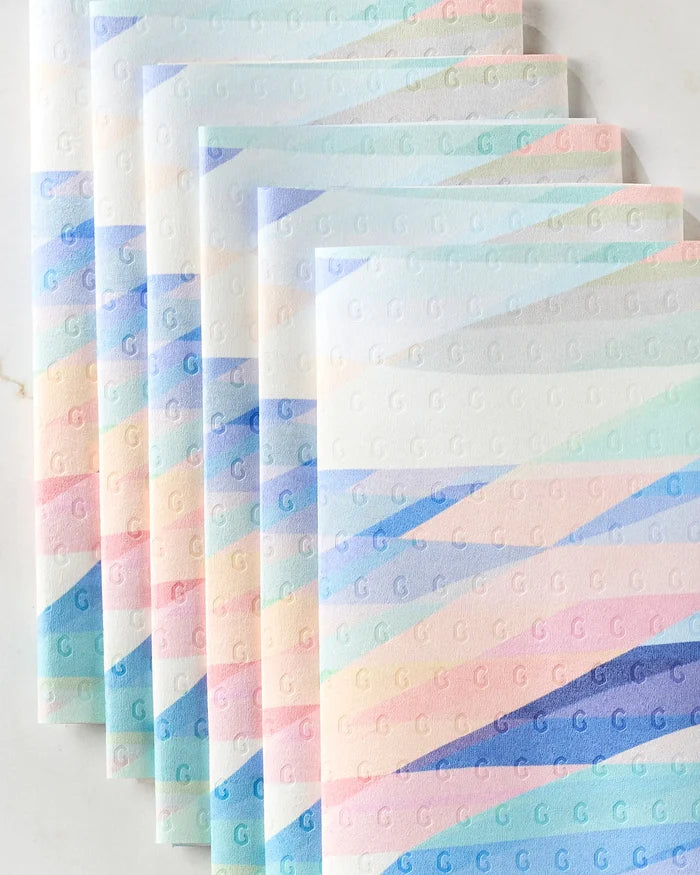 Five "Eventide" kitchen towels by Rachel Parker, featuring pastel diagonal stripes in blue, pink, and peach with embossed letter G patterns, are fanned out and slightly overlapping on a light surface.