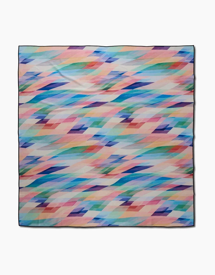The Eventide square scarf by Rachel Parker is made from recycled materials and showcases overlapping diamond patterns in pastel blue, pink, peach, green, and purple on a white background.
