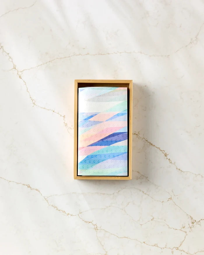 The Rachel Parker "Eventide" features a pastel geometric-patterned reusable cloth presented in a rectangular box, resting on white marble streaked with light brown veins.