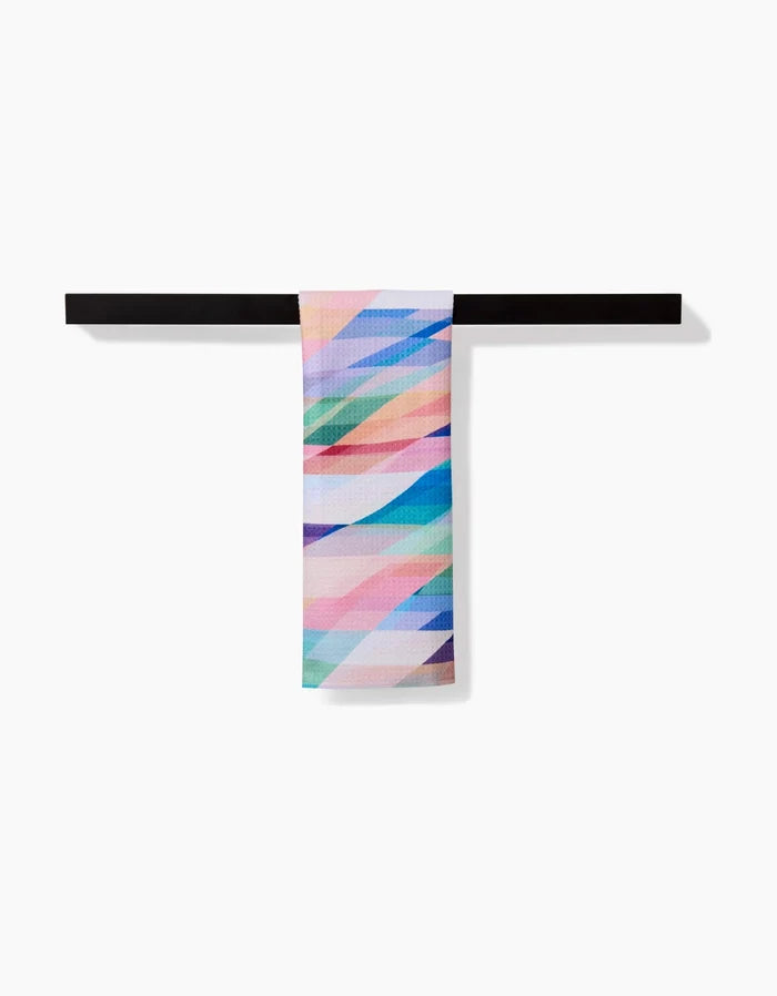 The Rachel Parker Eventide Bar Towel features diagonal pastel stripes in a geometric pattern on soft Geoweave fabric, shown draped over a black horizontal bar against a white background.