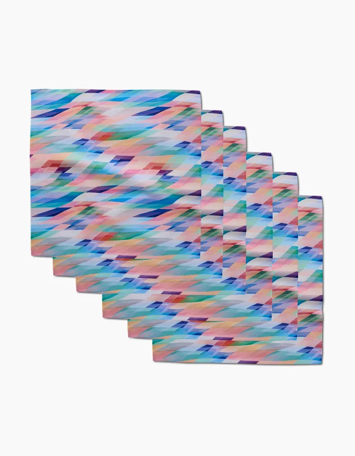 Six eco-friendly Eventide napkins by Rachel Parker, featuring a colorful abstract geometric pattern in blue, pink, green, orange, and purple on soft Geosuede fabric, are stacked on a white background.