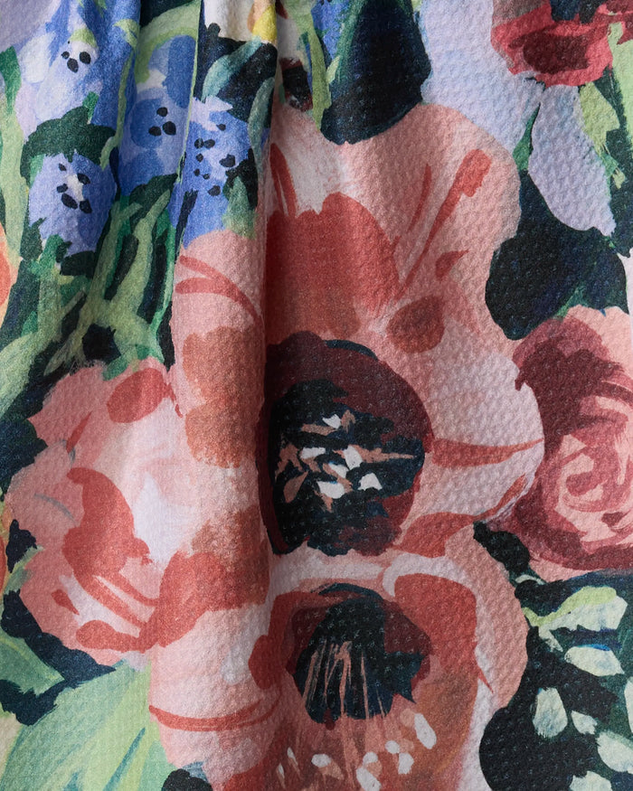 Close-up of Exotic Bouquet tea towel fabric by Ania Zwara Art, featuring a colorful floral pattern—large red, pink, and purple flowers with green leaves plus black, white, and blue accents. The top edge of the textured fabric appears slightly gathered.