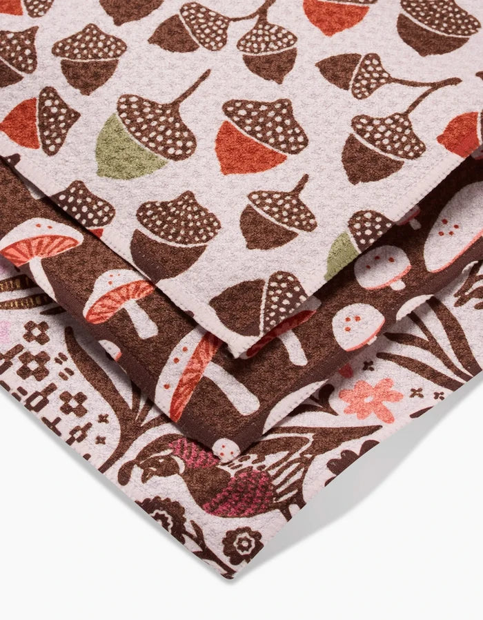 Kayla Ann’s Fall Abundance features three stacked Geoweave dishcloths with acorn, mushroom, and foliage patterns in earthy browns, reds, greens, and cream—stylish and eco-friendly, made from recycled materials.