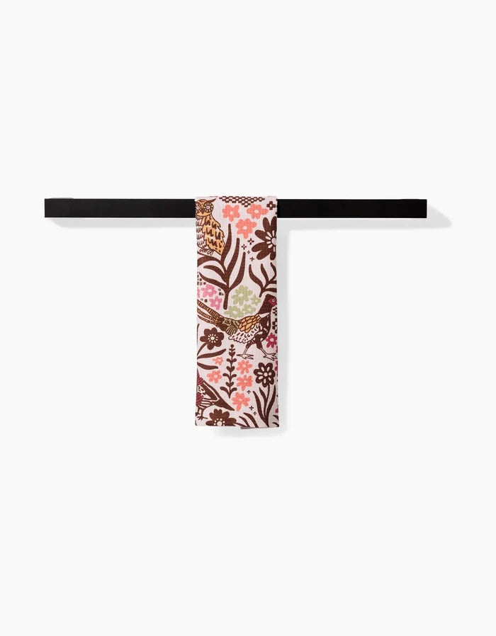 The Kayla Ann Fall Fowl towel, featuring a colorful floral and bird pattern in brown, pink, and green, hangs neatly on a black rod against a plain white background.