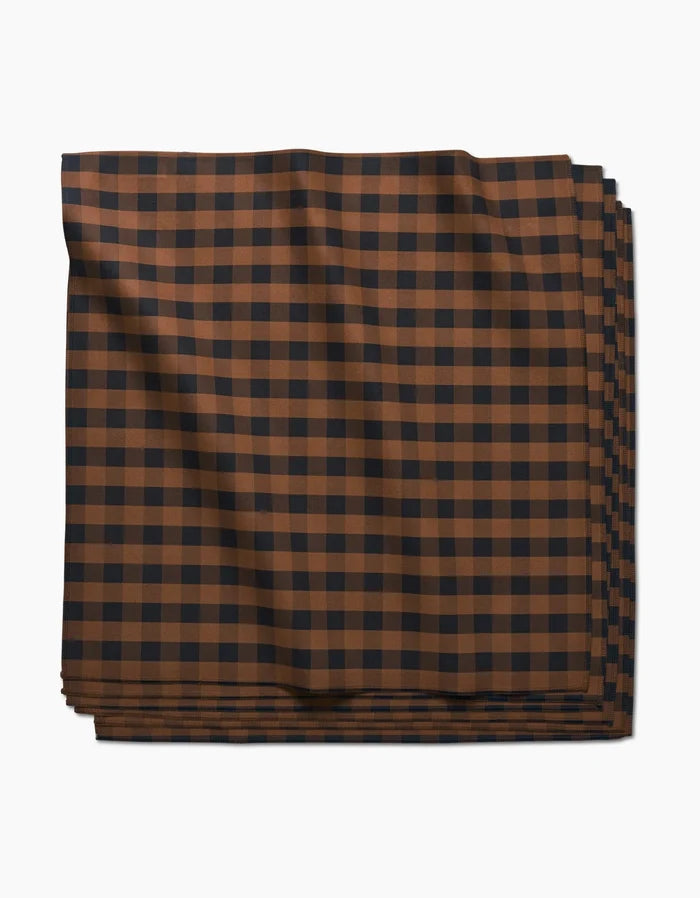 The Fall Gingham Dinner Napkin by GEOMETRY, crafted from Geosuede fabric, features a brown and black checkered pattern and is shown neatly folded against a white background.