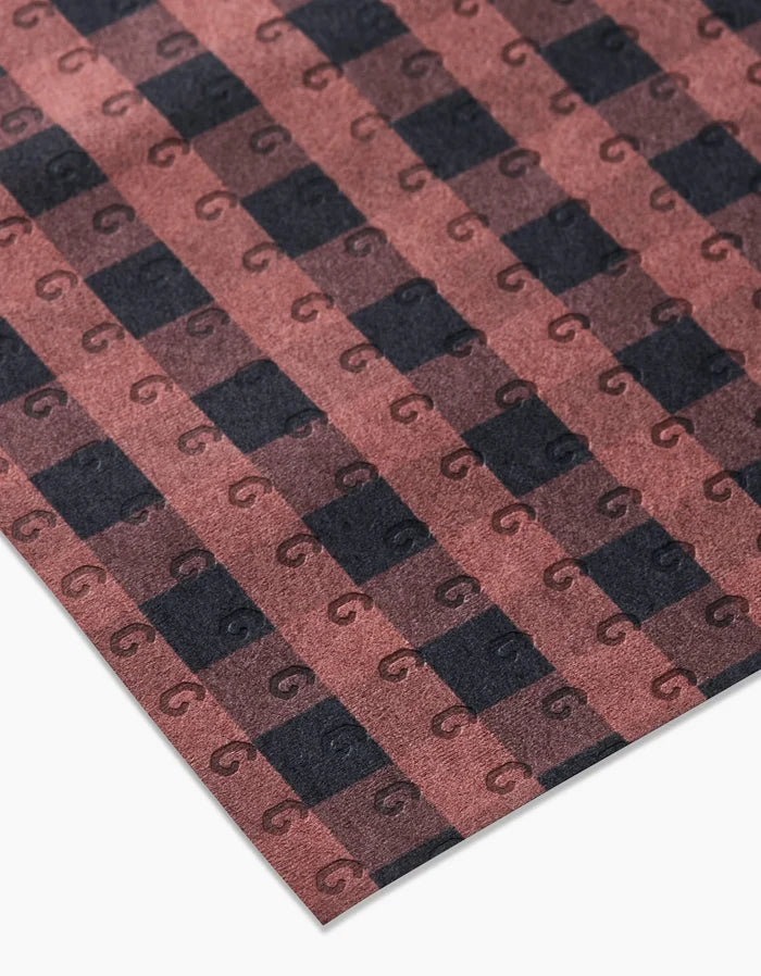 A close-up of GEOMETRY’s Fall Gingham reusable fabric, featuring a brown and black checkered pattern with small, dark “G” letters on each square—an eco-friendly alternative to paper towels.