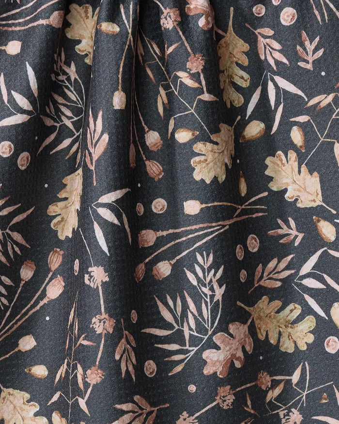 Close-up of Katie O'Shea's Fallen Oak: dark fabric made from recycled materials, featuring a scattered botanical pattern with light brown and beige leaves, acorns, and branches—perfect for a stylish kitchen or tea towel.