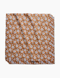 The Falling Acorns table linen by Charlie Rowan Designs features a brown background with a repeating white and black leaf pattern. This eco-friendly fabric is neatly folded and stacked, shown against a white backdrop.